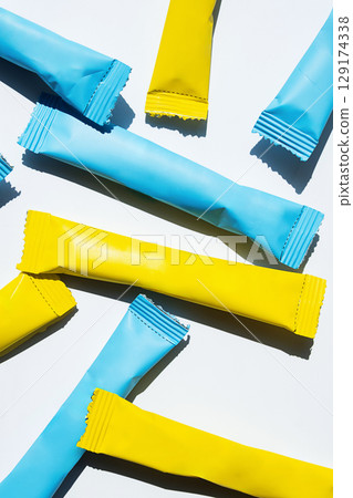 Yellow and blue stick pack sachets scattered on a white background. 129174338