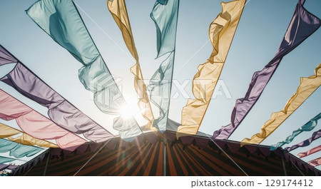 Colorful fabric banners flowing in wind against blue sky with sunburst 129174412