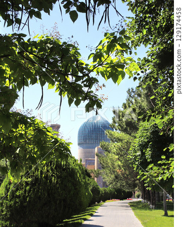 Famous landmark Gur Emir Mausoleum in Samarkand, Uzbekistan. Exterior of tomb of Amir Timur Tamerlan. Dome of Gur-e-Amir mausoleum of turco-mongol conqueror Timur. Focus on leaves in the foreground 129174458