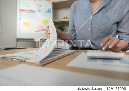 Remote Work. Professional woman analyzing data and using calculator in modern office. 129175008
