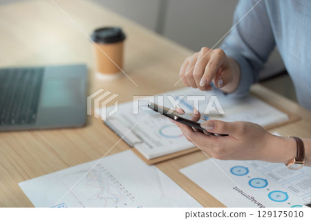 Remote Work. Woman using smartphone to review data in home office. 129175010