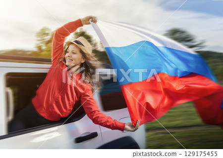 Woman celebrating Russia Day by waving the Russian flag from a car during a road trip, embodying pride and independence outdoors 129175455