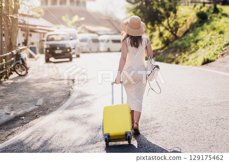 Wander Woman - Boho Clad Solo Traveler with Yellow Suitcase Strolling a Sunlit Summer Street -The Spirit of Independent Adventure 129175462