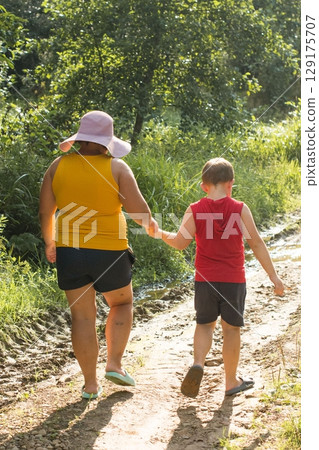 A woman and child stroll along a sun-drenched path, hand-in-hand, enjoying a leisurely walk in nature. A woman and child stroll along a sun-drenched path, hand-in-hand, enjoying a leisurely walk in nature. 129175707