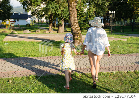 A mother and daughter stroll hand-in-hand through a park on a sunny day. A mother and daughter stroll hand-in-hand through a park on a sunny day. 129177104