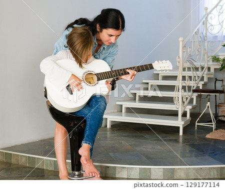 A mother teaches her daughter to play the acoustic guitar. A heartwarming moment of musical education and family bonding. 129177114