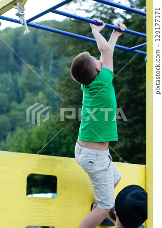 A child enthusiastically climbs a playground structure, showcasing physical strength and outdoor fun. A child enthusiastically climbs a playground structure, showcasing physical strength and outdoor fun. 129177171