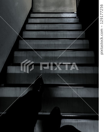 The feet of a man descending a dimly lit staircase The feet of a man descending a dimly lit staircase 129177256