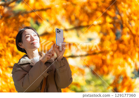 A woman taking pictures of autumn leaves with her smartphone Lifestyle image A woman taking pictures of autumn leaves with her smartphone Lifestyle image 129177360