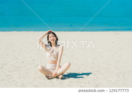 穿著泳衣的年輕女子坐在沙灘上 129177773