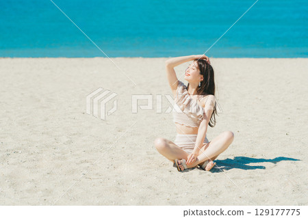 穿著泳衣的年輕女子坐在沙灘上 129177775