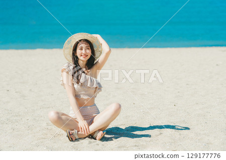 穿著泳衣的年輕女子坐在沙灘上 129177776