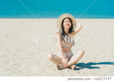 穿著泳衣的年輕女子坐在沙灘上 129177777