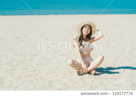穿著泳衣的年輕女子坐在沙灘上 129177778