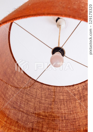 Close-up of a glowing ceiling pendant lamp with a natural straw shade. Warm interior lighting. 129178320