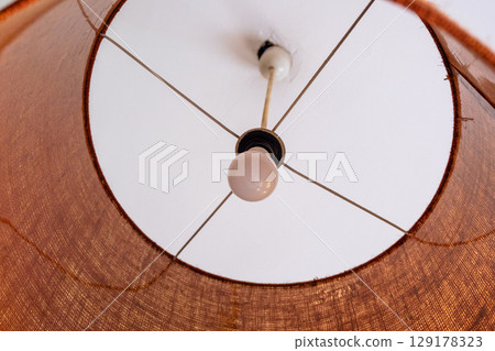 Close-up of a glowing ceiling pendant lamp with a natural straw shade. Warm interior lighting. Close-up of a glowing ceiling pendant lamp with a natural straw shade. Warm interior lighting. 129178323