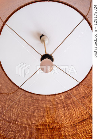Close-up of a glowing ceiling pendant lamp with a natural straw shade. Warm interior lighting. 129178324