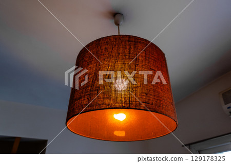 Close-up of a glowing ceiling pendant lamp with a natural straw shade. Warm interior lighting. 129178325