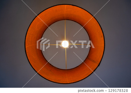 Close-up of a glowing ceiling pendant lamp with a natural straw shade. Warm interior lighting. Close-up of a glowing ceiling pendant lamp with a natural straw shade. Warm interior lighting. 129178328