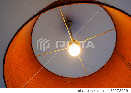 Close-up of a glowing ceiling pendant lamp with a natural straw shade. Warm interior lighting. 129178329