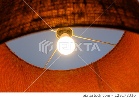 Close-up of a glowing ceiling pendant lamp with a natural straw shade. Warm interior lighting. Close-up of a glowing ceiling pendant lamp with a natural straw shade. Warm interior lighting. 129178330