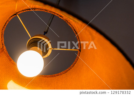 Close-up of a glowing ceiling pendant lamp with a natural straw shade. Warm interior lighting. 129178332