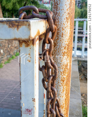 rusty chain is tied to a metal railing. Boat mooring. Reliable old chain. 129179052