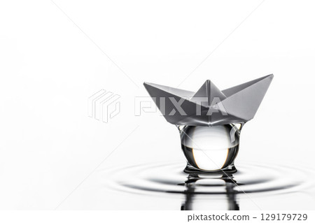 A paper boat on a drop of water that creates circles. Space for text. 129179729