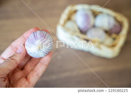 Female hand holding a head of Chinese single clove garlic with a basket full of garlic in the background. Natural food ingredient and kitchen preparation. 129180225