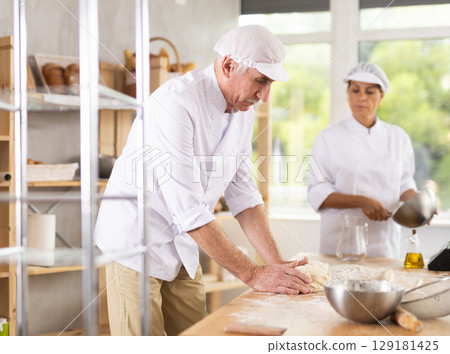 Elderly man and woman kneading and whipping dough 129181425