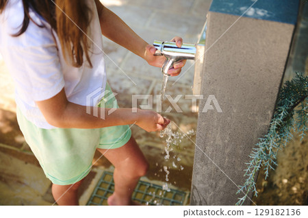 Young Girl Washing Hands at an Outdoor Water Tap on a Bright Sunny Day 129182136