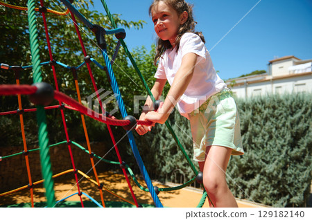 Smiling Girl Enjoys Outdoor Activity on Colorful Rope Playground on a Bright Sunny Day 129182140