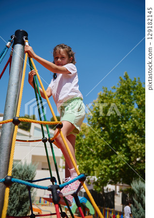 Young Girl Climbing Playground Rope Frame on a Clear Sunny Day 129182145
