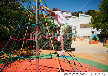 Child Climbing a Colorful Rope Pyramid in a Playground On a Bright Sunny Day 129182147