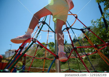 Child Climbing a Colorful Rope Structure in a Playground on a Sunny Day Child Climbing a Colorful Rope Structure in a Playground on a Sunny Day 129182149