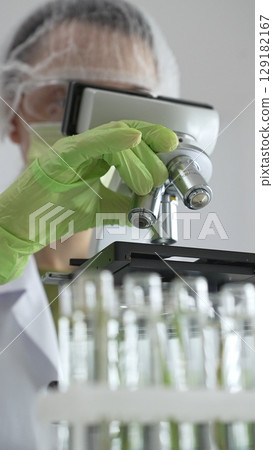 Close up of scientific precision involving green gloved hands adjusting microscope lens, blurred laboratory glassware highlighting medical investigation. Medicine, laboratory and science concept Close up of scientific precision involving green gloved hands adjusting microscope lens, blurred laboratory glassware highlighting medical investigation. Medicine, laboratory and science concept 129182167