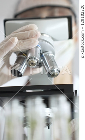 Close up of white gloved hand of a scientist adjusting a microscope in a laboratory. Medicine, health care and science concept 129182220