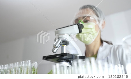 Scientist analyzing test tubes, wearing green protective gear while working with microscope in sterile laboratory research environment. Medicine, healthcare and science concept 129182246