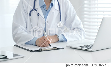 Female doctor documents patient information while working with digital devices at workplace in office. Medicine and healthcare concept Female doctor documents patient information while working with digital devices at workplace in office. Medicine and healthcare concept 129182249