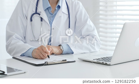 Female doctor documents patient information while working with digital devices at workplace in office. Medicine and healthcare concept Female doctor documents patient information while working with digital devices at workplace in office. Medicine and healthcare concept 129182250