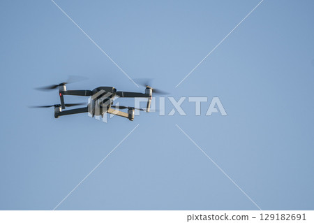 Modern RC Drone / Quadcopter with camera flying at sunrise. Modern RC Drone / Quadcopter with camera flying at sunrise. 129182691