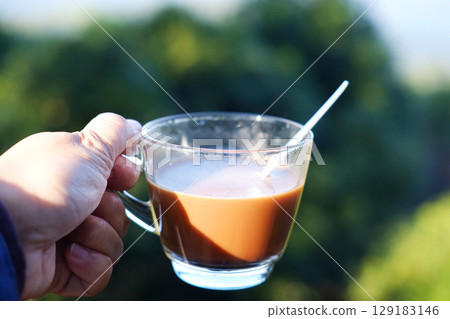 Close up hand holding a glass cup of hot coffee on the valley mountain in natural sunlight of morning bright day 129183146