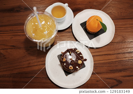 Homemade fresh Chocolate Hazelnut cake with orange cake and cream on chocolate Hazelnut and orange juice with a cup of hot tea on wooden table. top view Homemade fresh Chocolate Hazelnut cake with orange cake and cream on chocolate Hazelnut and orange juice with a cup of hot tea on wooden table. top view 129183149