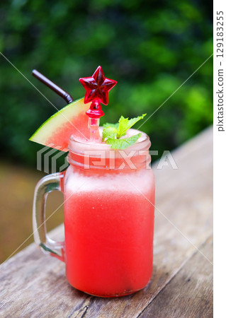 A glass of watermelon smoothie with red star spoon on wooden table in tropical of cafe. Copy space of vertical photo 129183255