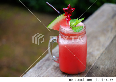 A glass of watermelon smoothie with red star spoon on wooden table in tropical of cafe. Copy space 129183256