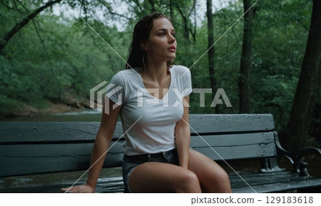 Young woman sitting on bench with her hair wet. She is wearing white T-shirt 129183618