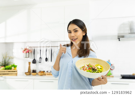 Young Woman Cooking in the kitchen. Healthy Food - Vegetable Salad Diet. Healthy Lifestyle. Cooking delicious food during the COVID-19 self-quarantine 14 days. Stay at home concept. 129183962