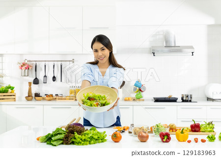 Young Woman Cooking in the kitchen. Healthy Food - Vegetable Salad Diet. Healthy Lifestyle. Cooking delicious food during the COVID-19 self-quarantine 14 days. Stay at home concept. 129183963