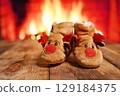 small fleece boots with the head of a Christmas deer in front of a fireplace 129184375