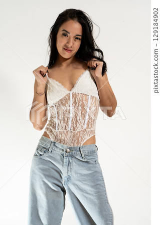 Young latin woman pulling her white bodysuit straps while posing in studio Young latin woman pulling her white bodysuit straps while posing in studio 129184902